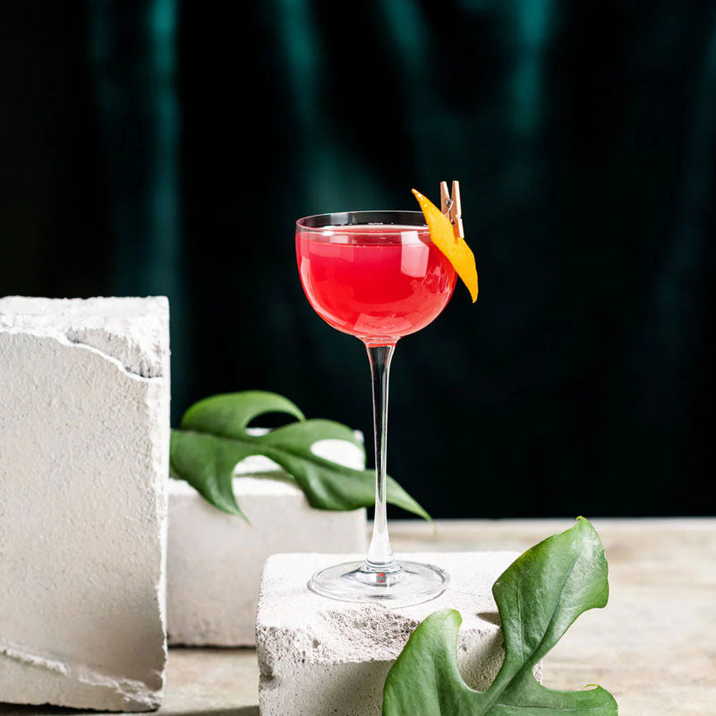 Ginger Cosmo cocktail served in a Nick & Nora glass with a garnish of orange peel on a textured surface.