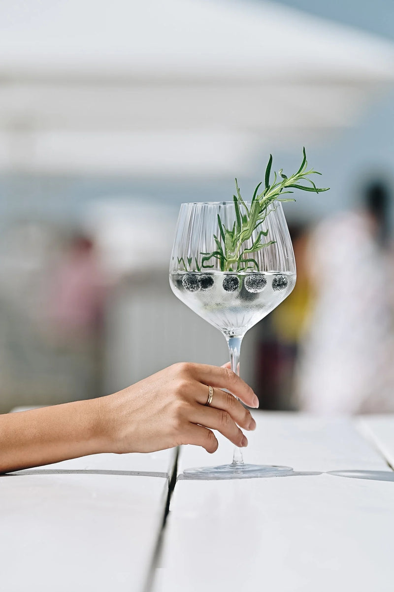 It's Botaniets o'Knokke cocktail garnished with herbs in a beautiful glass by the beach.