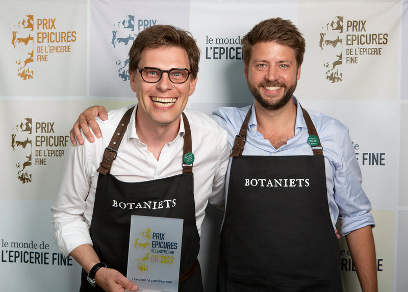 Two smiling men in Botaniets aprons celebrating the Golden Epicure in Paris with an award.