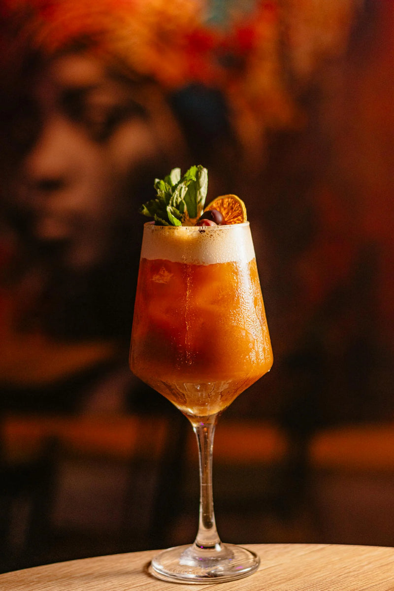 A refreshing La Flamme (Paris 2024) mocktail garnished with mint and dehydrated orange, set against a colorful background.