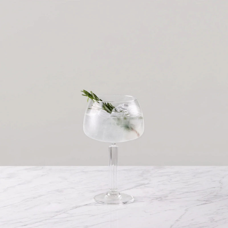 Elderflower tonic cocktail garnished with rosemary in a stylish glass on a marble surface.