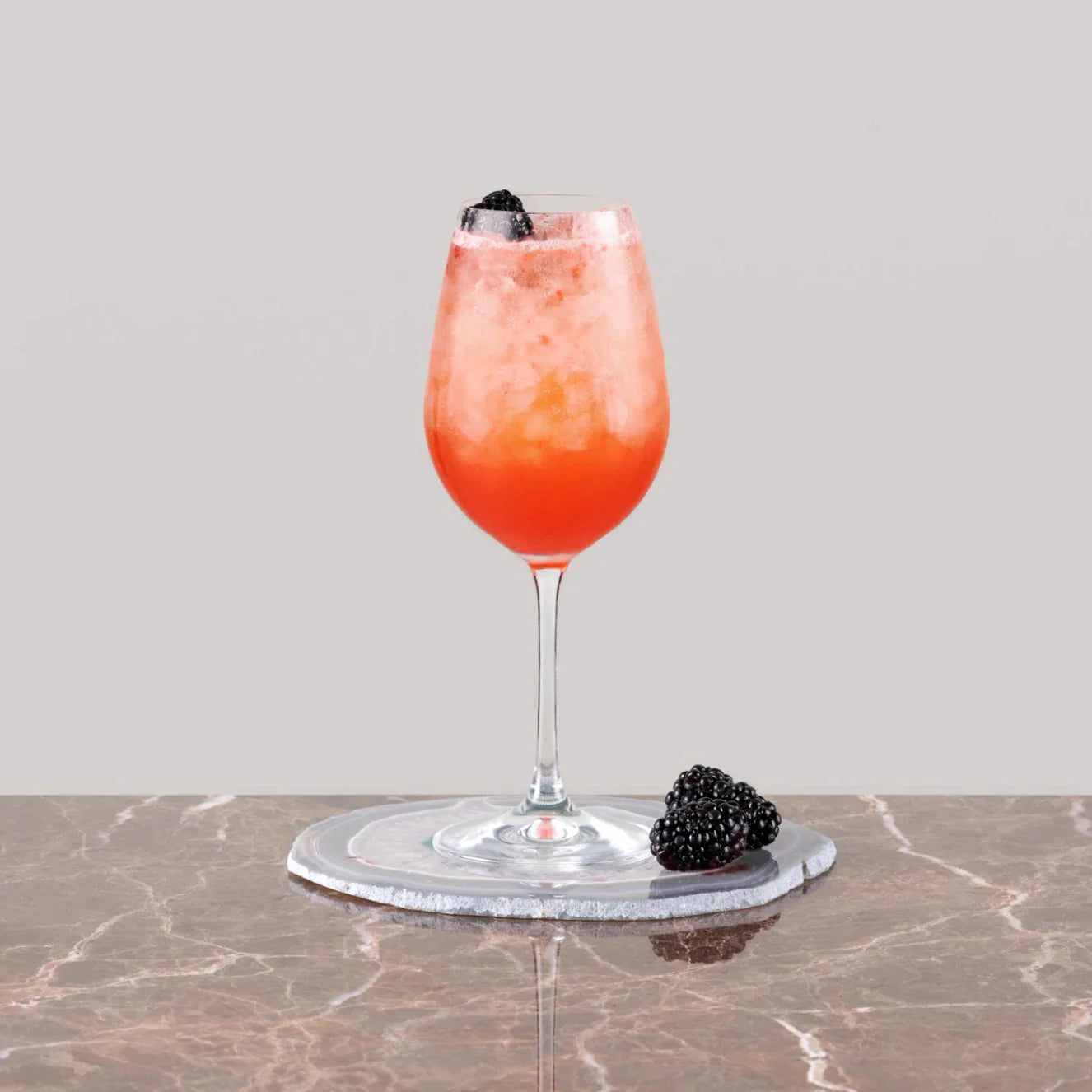 Refreshing Ostend Fizz cocktail served in a wine glass with ice and blackberries on a marble surface.