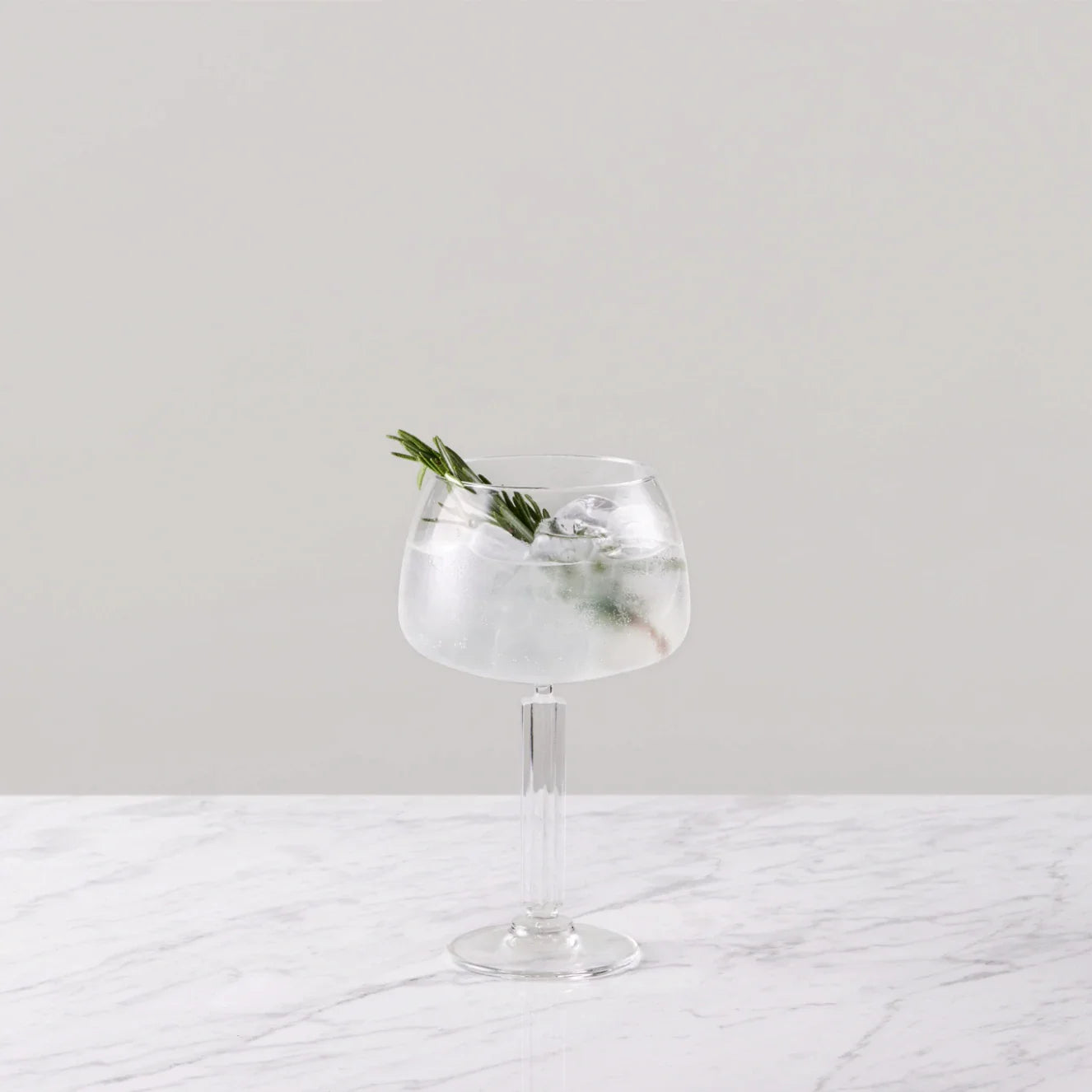 Elderflower tonic cocktail garnished with rosemary in a stylish glass on a marble surface.