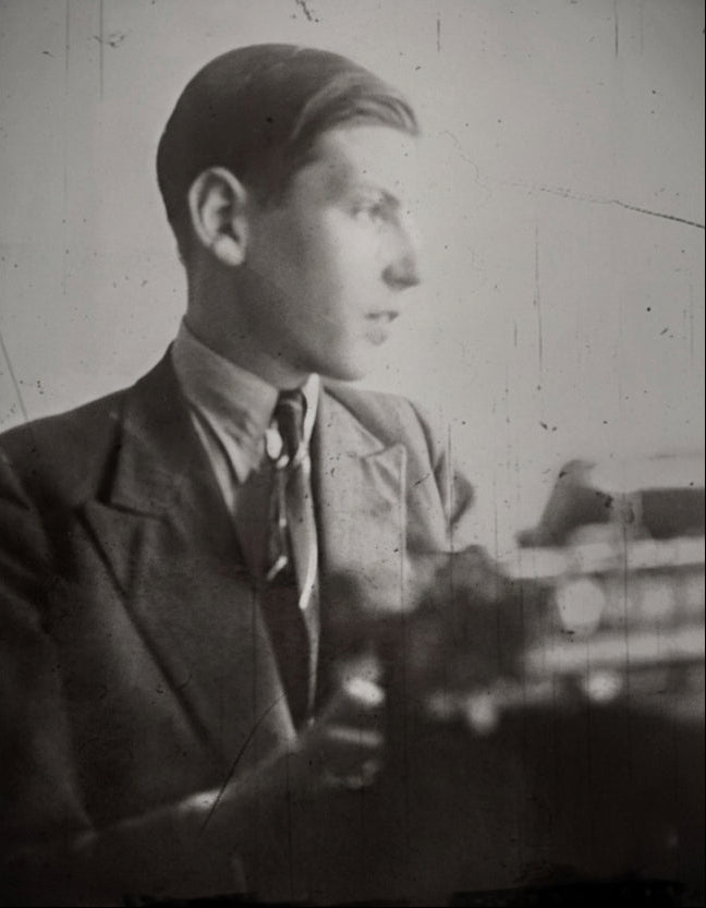 Vintage black and white photo of a person sitting at a desk with a typewriter.